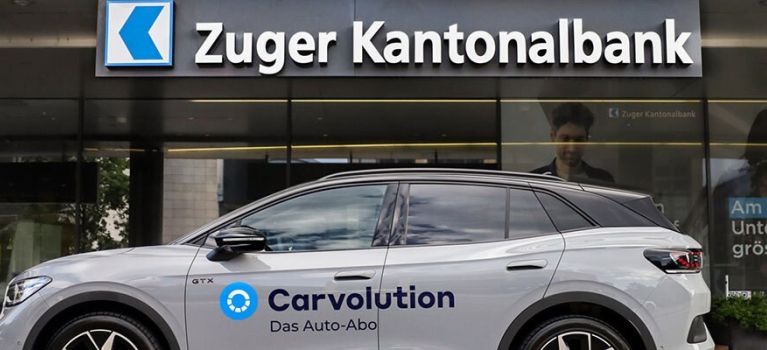 VW ID.4 GTX portant la marque Carvolution devant une banque cantonale de Zug